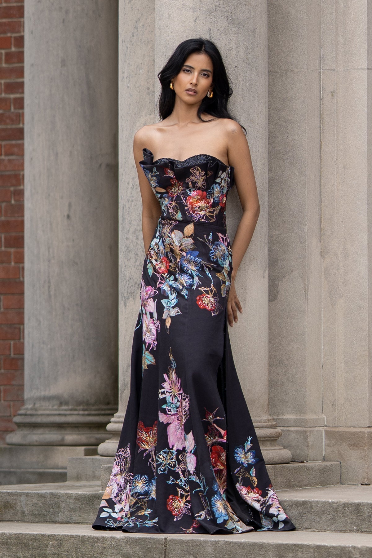 Ranna Gill’s Sera Gown in black viscose jacquard with strapless ruffle neckline, floral print, thigh-high slit, and sequin detailing.