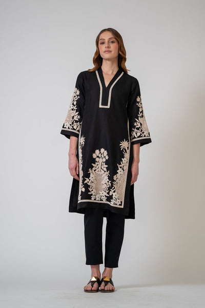 Woman wearing a black embroidered kurta with white patterns on a plain background