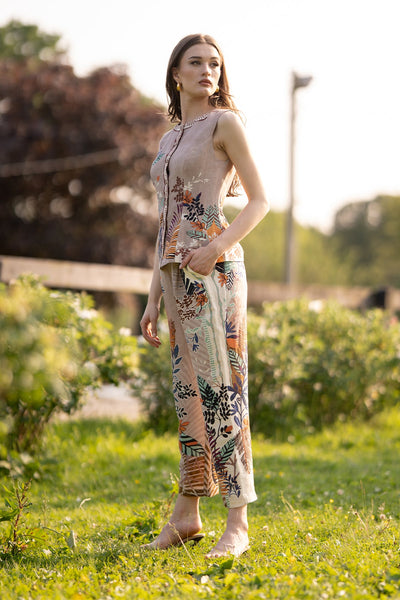 Side view of Ranna Gill Liora Rara Pants in beige linen-viscose fabric with vibrant tropical botanical prints in orange, green, blue, and black, featuring straight fit and elastic waistband.