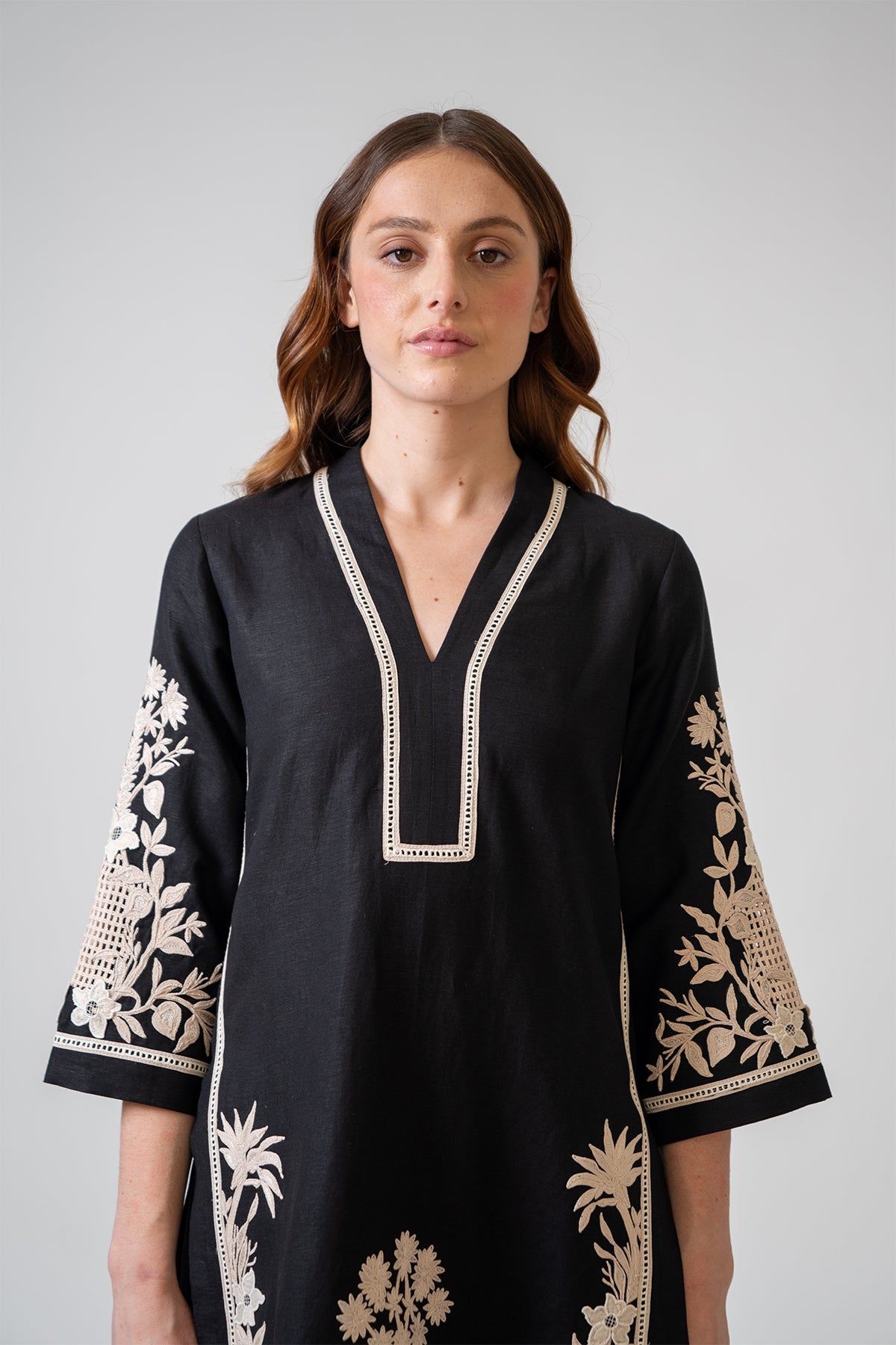 Woman wearing a black dress with white embroidery on a gray background