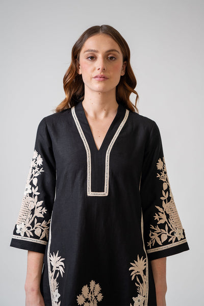 Woman wearing a black dress with white embroidery on a gray background