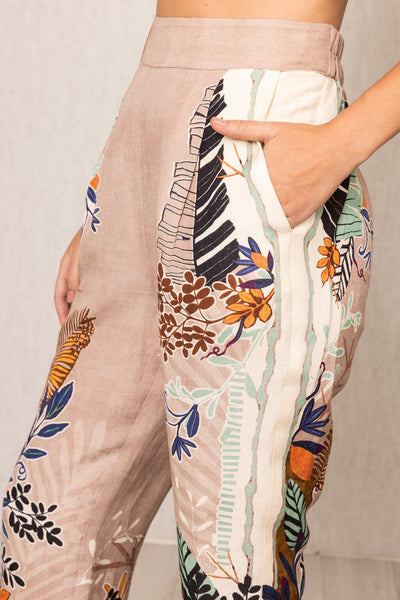 Closer view of Ranna Gill Liora Rara Pants in beige linen-viscose fabric with vibrant tropical botanical prints in orange, green, blue, and black, featuring straight fit and elastic waistband.