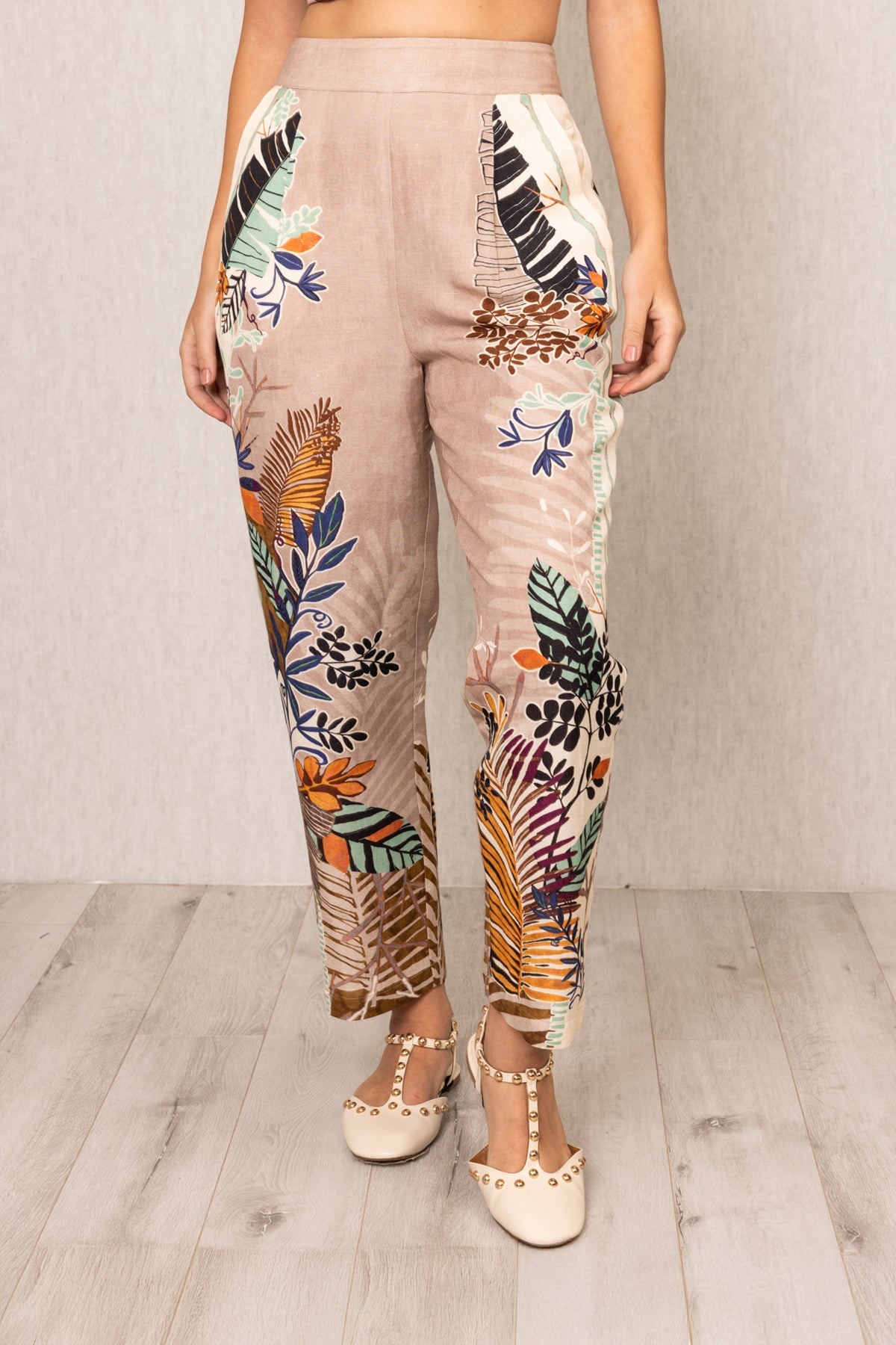 Front view of Ranna Gill Liora Rara Pants in beige linen-viscose fabric with vibrant tropical botanical prints in orange, green, blue, and black, featuring straight fit and elastic waistband.