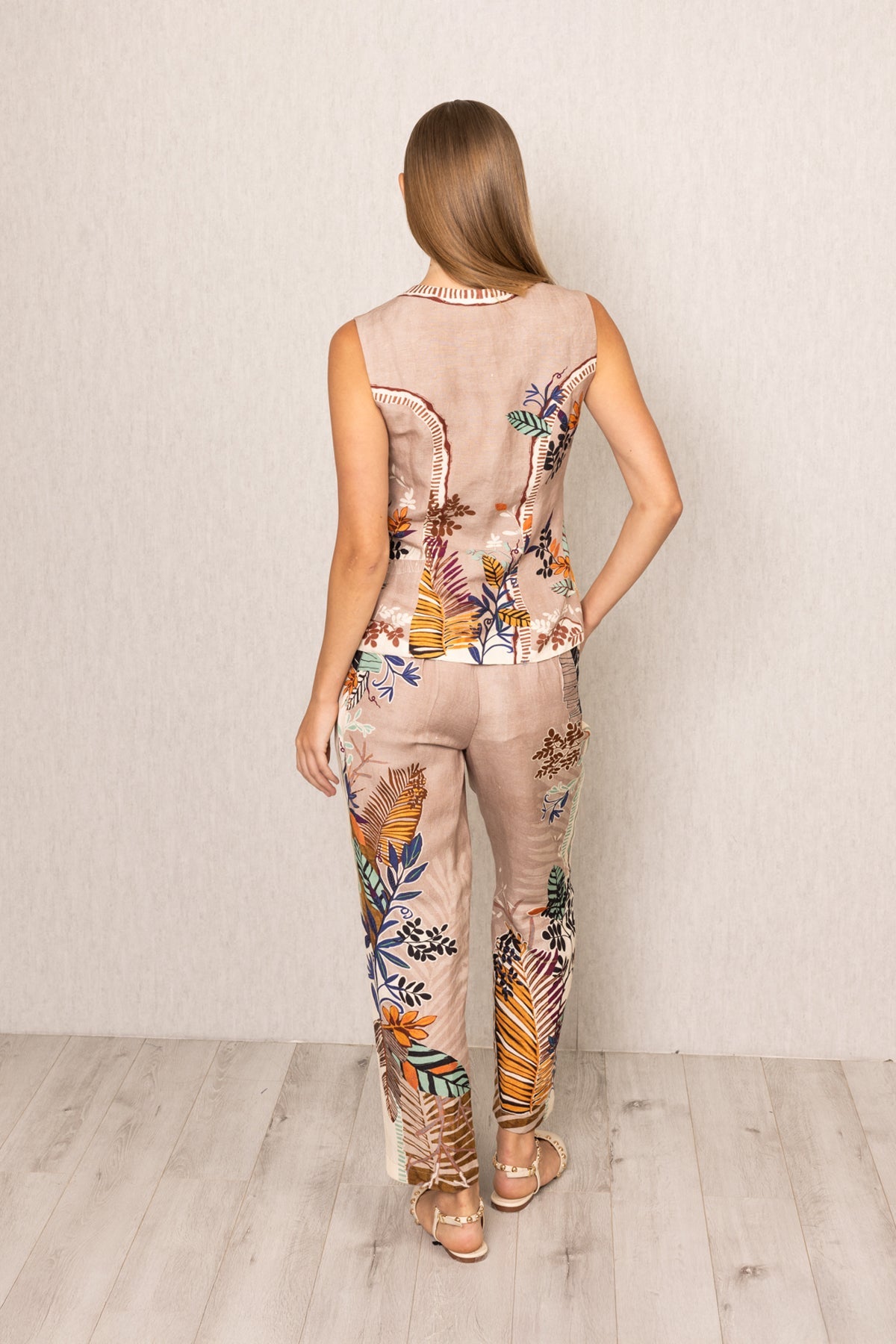 Back view of Ranna Gill Liora Rara Pants in beige linen-viscose fabric with vibrant tropical botanical prints in orange, green, blue, and black, featuring straight fit and elastic waistband.