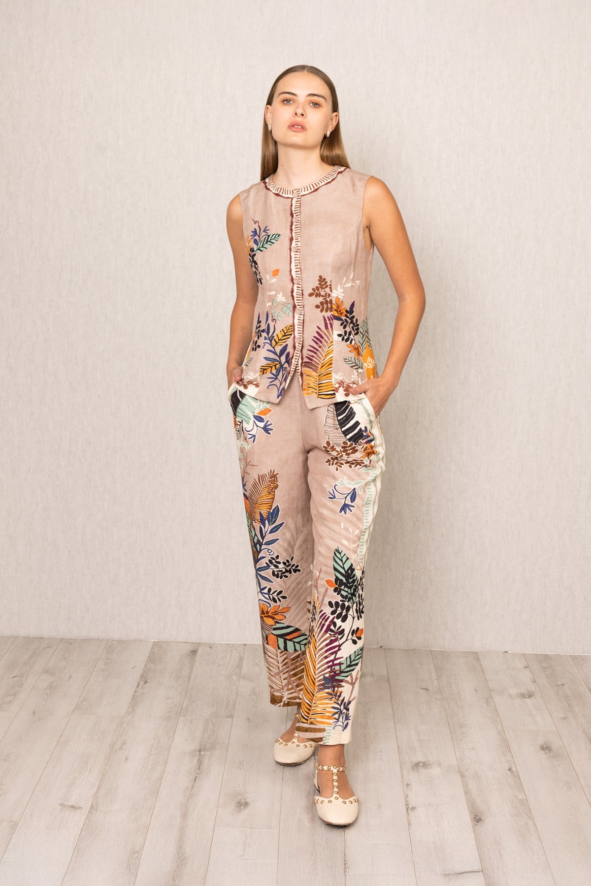 Front view of Ranna Gill Liora Rara Pants in beige linen-viscose fabric with vibrant tropical botanical prints in orange, green, blue, and black, featuring straight fit and elastic waistband.