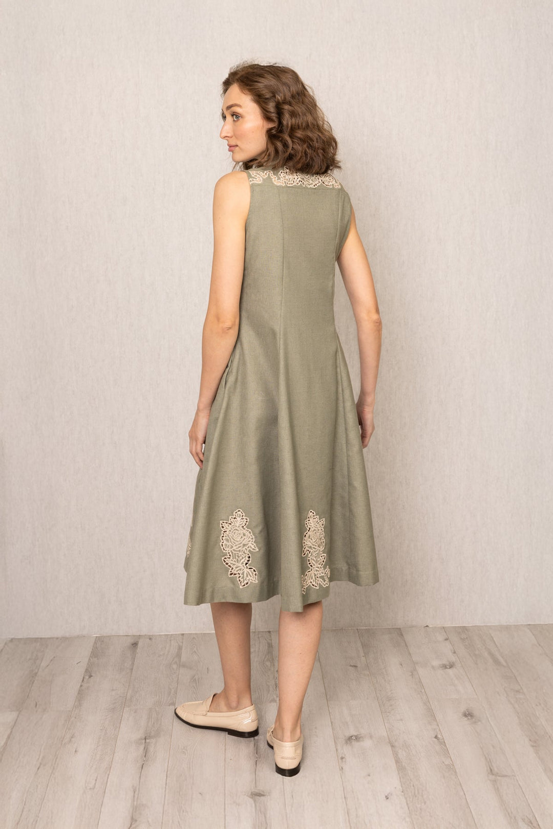 Woman wearing a sleeveless green dress with lace details on a plain background