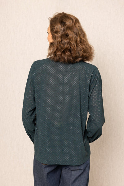 Person wearing a teal long-sleeve top with a subtle pattern against a beige wall.