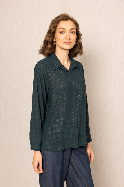 Woman wearing a dark green patterned shirt against a beige background