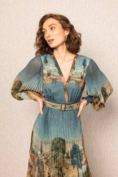 Woman wearing a blue pleated dress with a belt against a beige background