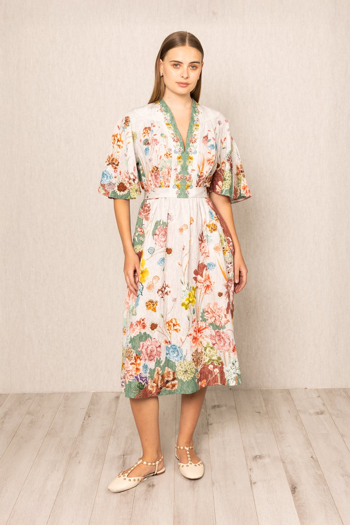 Woman wearing a floral V- neck dress standing against a plain background