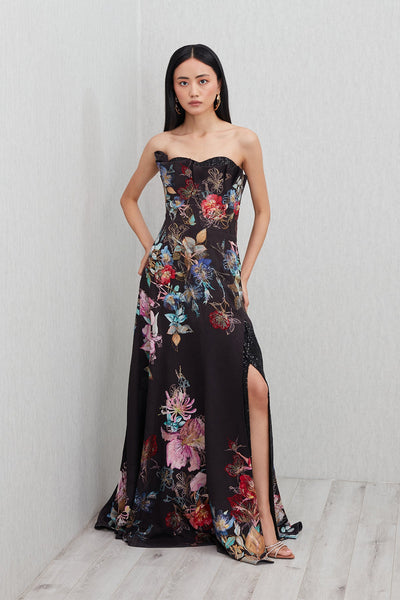 Ranna Gill’s Sera Gown in black viscose jacquard with strapless ruffle neckline, floral print, thigh-high slit, and sequin detailing.