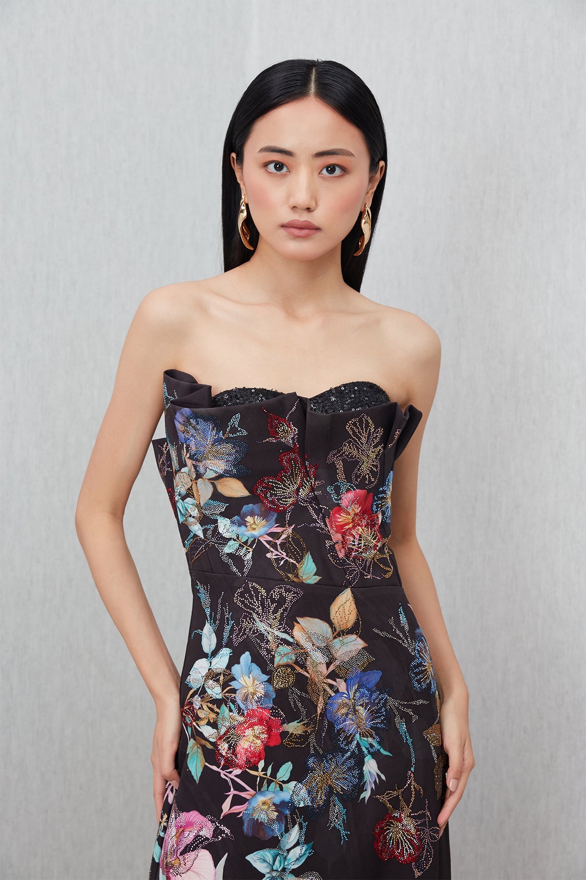 Ranna Gill’s Sera Gown in black viscose jacquard with strapless ruffle neckline, floral print, thigh-high slit, and sequin detailing.