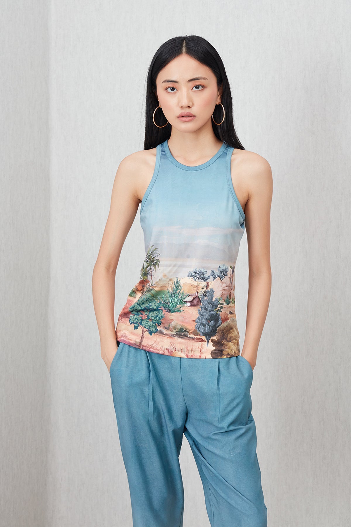 Woman wearing a sleeveless top with a nature print and matching pants on a plain background