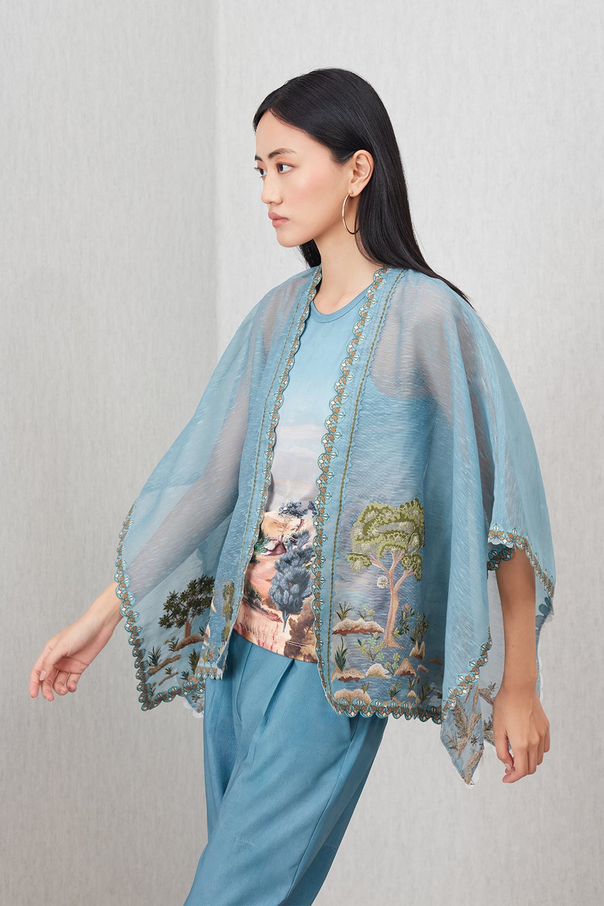 Woman wearing a light blue kimono-style garment with nature-themed embroidery on a plain background