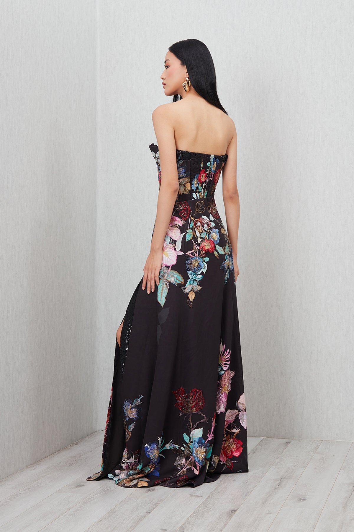 Ranna Gill’s Sera Gown in black viscose jacquard with strapless ruffle neckline, floral print, thigh-high slit, and sequin detailing.